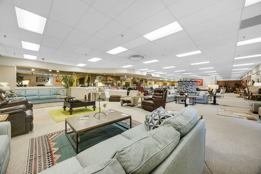 Wide showroom view with open carpeted floor, suspended ceiling and recessed lighting throughout.